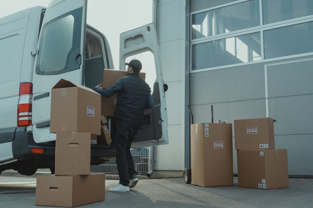 pexels photo 6169056 A delivery man unloading cardboard boxes from a van at a warehouse during the day.